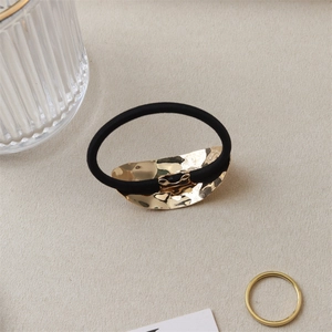 Detail of black elastic hair tie with hammered gold metal charm on beige fabric background