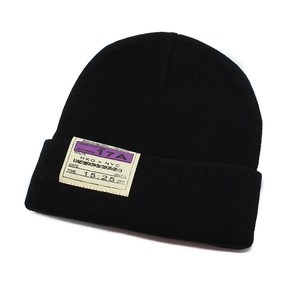 Close-up of black knitted beanie featuring industrial flight boarding pass patch detail