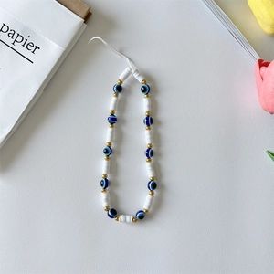 Detail of beaded phone strap with evil eye charms and pearls on white leather background