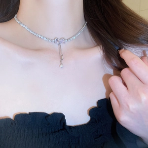 Close-up of zircon bow pendant with pearl tassels on a sparkling silver neck chain
