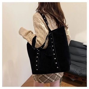 Side view of large black faux suede tote bag with metal studs and heart charm on model