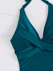 Detail of teal halter neck swimsuit featuring a cross-over twist design on marble background