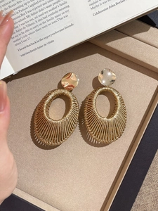 Macro detail of gold velvet braided oval earrings with metal weave on an open magazine