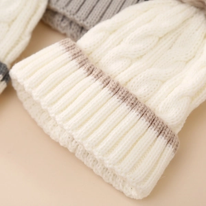 Close-up of white cable-knit baby winter hat with soft textured wool and brown trim