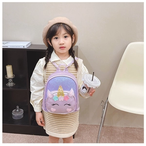 Toddler girl wearing a purple sequin unicorn backpack in a cozy indoor setting
