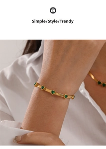 Detail of golden snake chain bracelet with five green heart-shaped gemstones on wrist