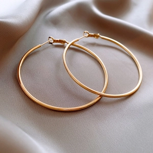 Detail of high-polish gold hoop earrings resting on elegant champagne silk fabric