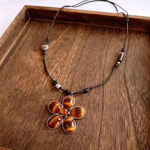 Detailed close-up of tiger eye stone flower pendant on black braided rope necklace