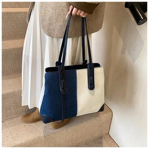 Detail of color-block denim tote bag with leather handles shown on a staircase