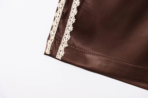 Close-up of brown satin shorts featuring white lace trim and detailed stitching