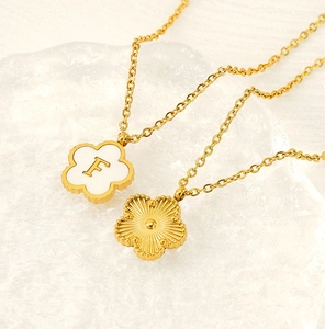 Detail shot of a gold five-petal flower pendant necklace with shell letter F engraving