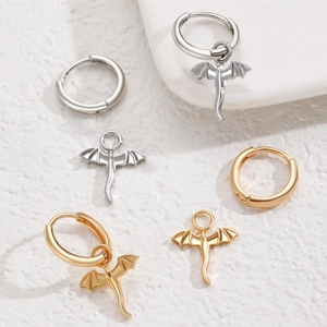 Macro detail of gold and silver dragon pendant earrings on a textured white background