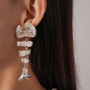 Detailed close-up of a silver fishbone earring with ornate swirl textures on a model