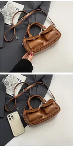 Detail view of mini brown leather saddle bag showing pockets and size comparison with phone