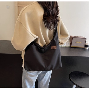 Black canvas tote bag featuring dual front pockets and brown leather brand label detail