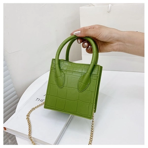 Detail of green mini crossbody bag with crocodile texture and gold chain strap