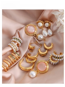 Detail of vintage gold-plated earrings with emerald zircon and pearls on pink silk fabric