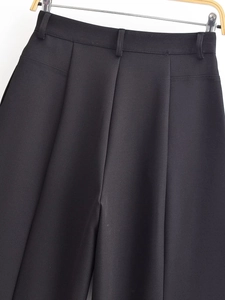 Détail d'un pantalon noir taille haute avec doubles plis et passants de ceinture