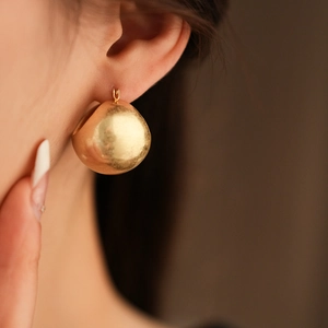 Close-up of golden teardrop metal hoop earrings with brushed texture on a model