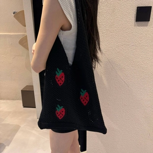 Detail of black crochet tote bag featuring red strawberry knit patterns worn by a model