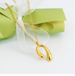Detail of gold U-shaped horseshoe pendant necklace with polished mirror finish on white silk