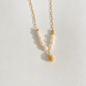 Detailed shot of irregular white pearls and a gold teardrop pendant on a gold chain