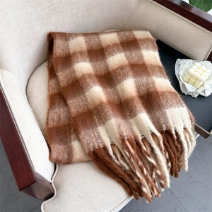 Winter plaid scarf in brown and beige with tassels draped over a cozy armchair