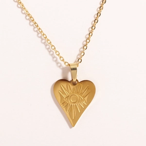 Detail shot of a gold heart pendant with an eye engraving on a stainless steel chain