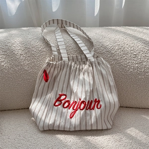 Detail of striped canvas tote bag with red Bonjour embroidery on soft texture