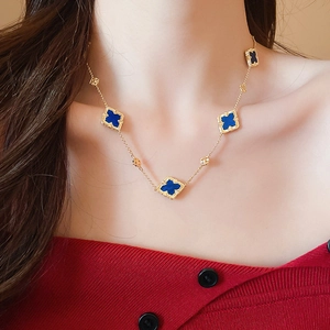 Detail of gold-plated clover necklace with five blue stones worn on a red top
