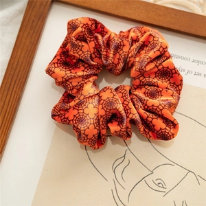 Detailed close-up of an orange velvet scrunchie with black spider web patterns for Halloween