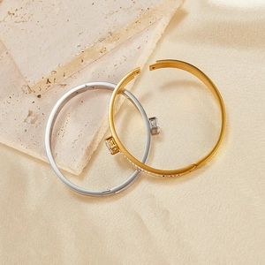 Detailed view of gold and silver hinged bangles with square zircon on beige fabric