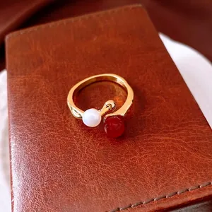 Vergoldeter offener Ring mit Süßwasserperle und roter Achatperle auf Ledertextur