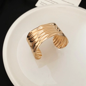 Close-up of wide gold open cuff bracelet with unique irregular wavy textured surface