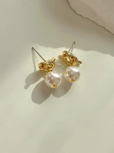 Detailed close-up of golden knot earrings with elegant round white pearls on a soft background