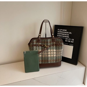 Detail of green and brown plaid tote bag with leather straps and metal buckle accent