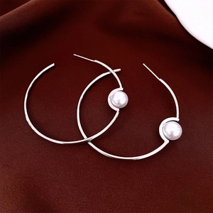 Detail view of large circular pearl hoop earrings on luxury dark red silk fabric