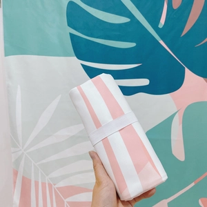 Pink and white striped quick-dry microfiber beach towel rolled with elastic storage band