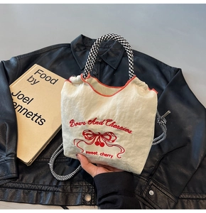 Detailed embroidery of red bows and cherries on a cream nylon tote bag with red stitching