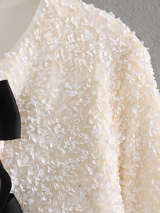 Detail of ivory sequin top with a decorative black grosgrain bow on the side fabric