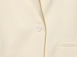 Détail du blazer crème montrant le tissu texturé, le bouton en résine et la poche passepoilée