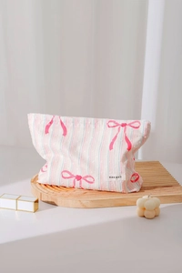 Pink striped cotton makeup bag with bow patterns and zipper on a wooden tray detail