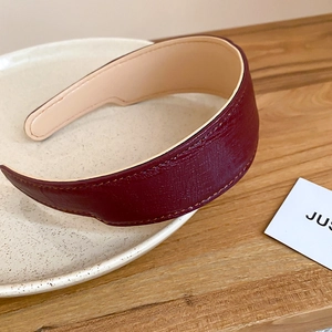 Detail of burgundy pleated leather headband with soft inner lining on a ceramic tray