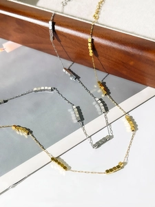 Close-up of minimalist gold and silver 18K square bead necklaces on a wooden tray