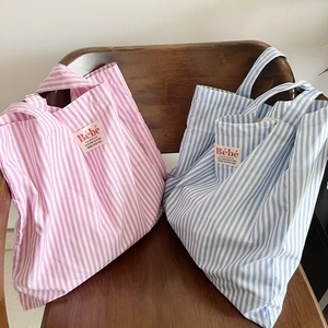 Dettaglio di borse tote in tela a righe rosa e blu con etichette Bebe su una sedia di legno