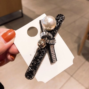 Close-up of black bow hair clip featuring rhinestones, clear crystals and faux pearls