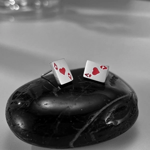 Detailed view of silver heart Ace poker card earring on a smooth dark stone base