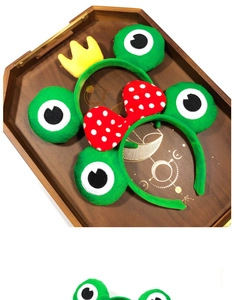 Détail de bandeaux grenouille en peluche avec nœud à pois rouges et couronne sur plateau