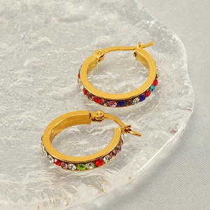 Dettaglio di orecchini a cerchio dorati con zirconi colorati su un vassoio di vetro chic