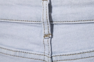 Macro shot of light blue denim jeans waist with reinforced stitching and belt loop details